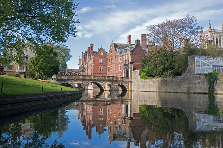 St John's College, Cambridge, with the Kitchen Bridge mirrored in the calm river under a blue sky — stock photography by Jean-Luc Benazet.