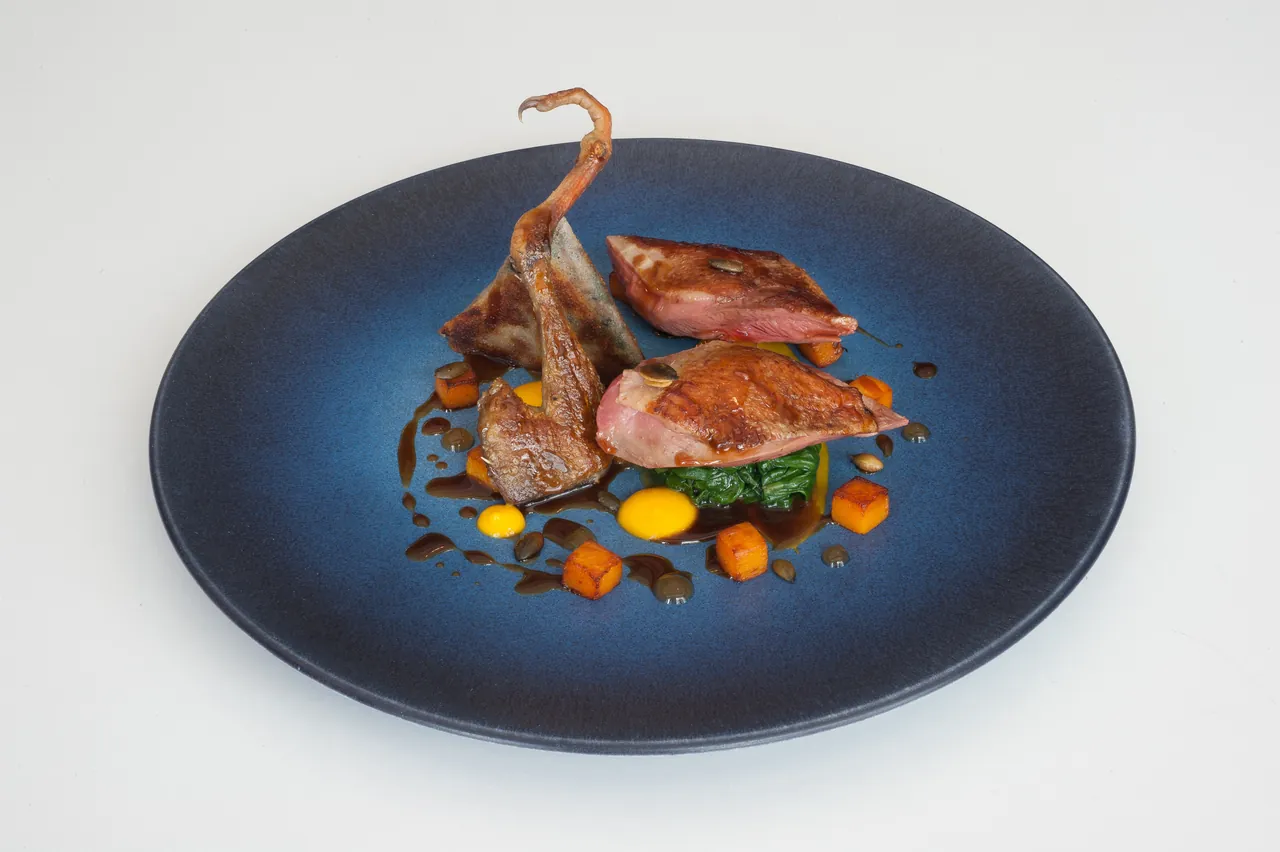 A plated quail dish on a dark blue plate, photographed from above